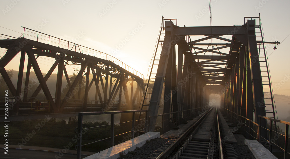 A railway bridge in the morning fog or smoke through which the rays of the sun shine