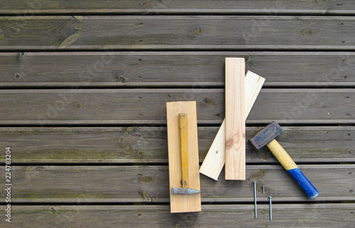 Three small wooden boards, three nails of different sizes and two hammers on a wooden terrace. Different tools on a wooden background. Hand working tools view from above.
