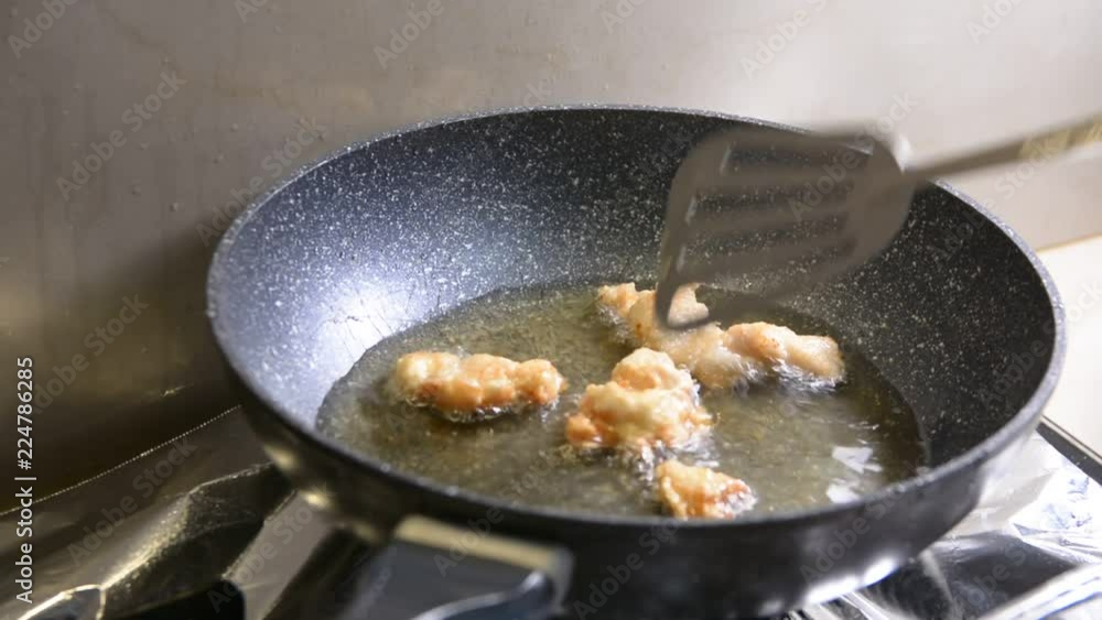 breaded chicken pieces being deep fried in a cast iron pan breaded chicken pieces being deep fried in a cast iron pan