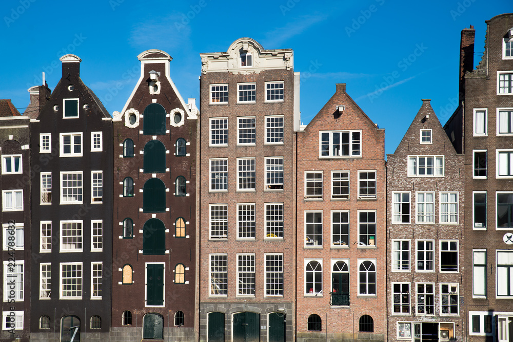 Houses in Amsterdam Netherlands, in straight symmetrical order. Skies are blue during the summer months. Famous landmark the represents the area. 