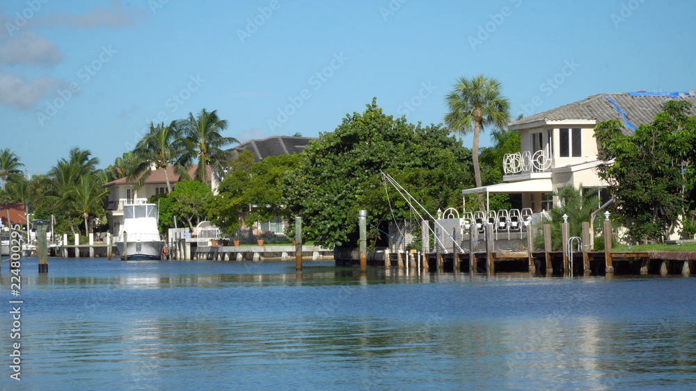 Fototapeta premium Day time view of coastal inlet in tropical island location with homes and private boat docks on river. Luxury expensive summer vacation homes