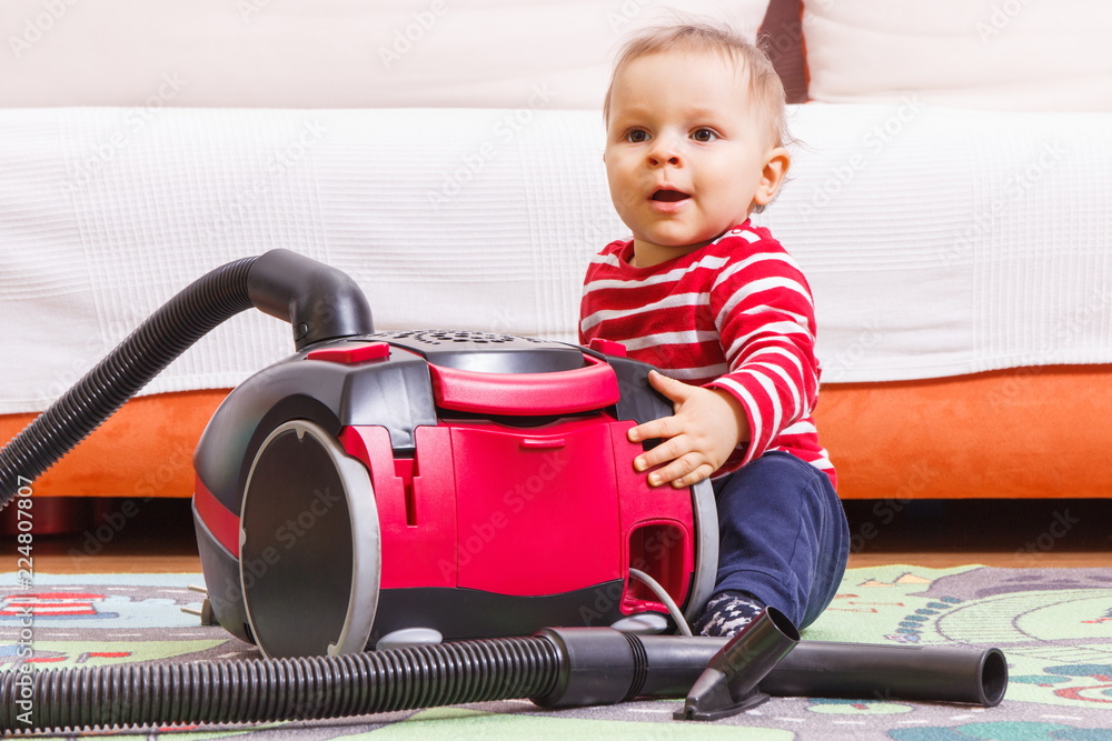 Happy little baby boy on carpet at home and vacuum cleaner with accessories Happy little baby boy on carpet at home and vacuum cleaner with accessories