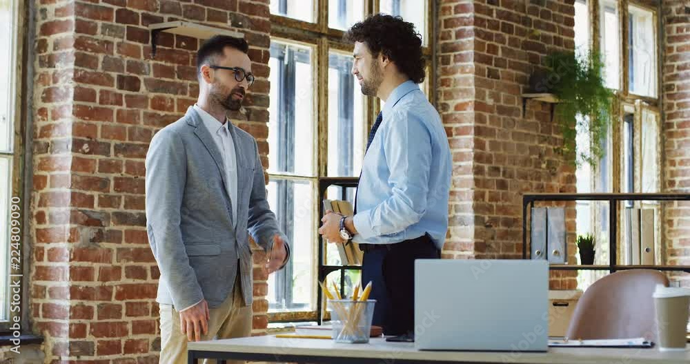 Two handsome caucasian man in the business style standing and having a talk in the loft style office. Two handsome caucasian man in the business style standing and having a talk in the loft style office.