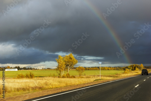 asphalt road among the fields and forests illuminated by the sun, the sky with textured clouds and clouds and a rainbow © Светлана Михалева