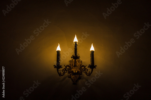 Golden electric candlestick with three candles at night in the dark with shadows on the yellow wall.