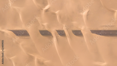 Photography Aerial view of a desert road being run over by sand dunes photographed from a drone at sunrise