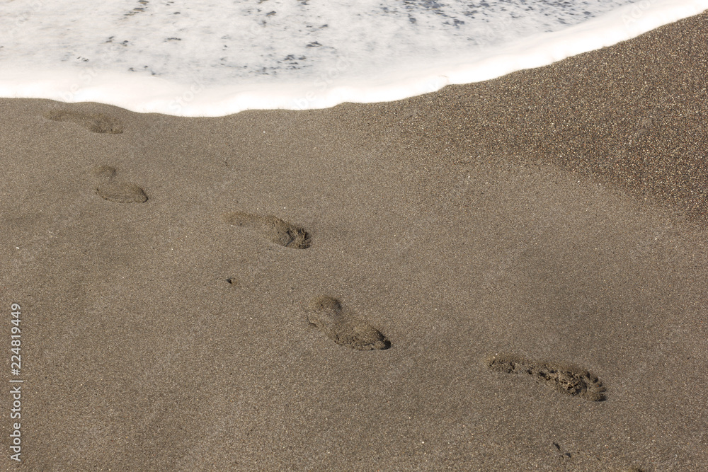 the background image is white the sea foam of the waves lapping on the sandy beach, washing away the footprints in the sand the background image is white the sea foam of the waves lapping on the sandy beach, washing away the footprints in the sand