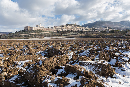 View of Assisi town (Umbria) in winter, with a field covered by snow and a blue sky with white clouds