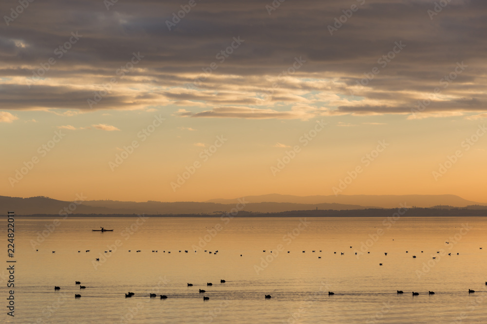 Beautiful view of a lake at sunset, with orange tones, birds on water and a man on a canoe