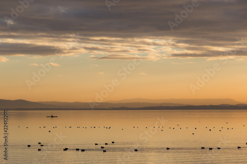 Beautiful view of a lake at sunset  with orange tones  birds on water and a man on a canoe