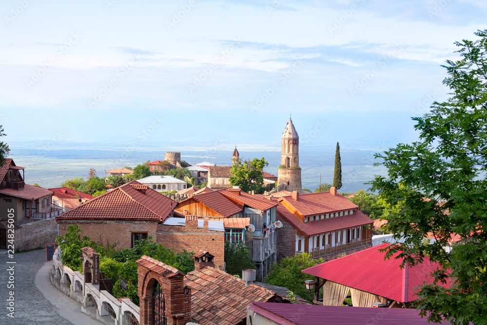 Sighnaghi city of love in Georgia, Kakheti region, red roofs of houses and brick towers of the cathedral and fortress, stone road, horizon, blue sky and green trees background