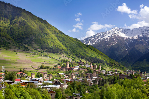 Ushguli village in Georgia, Svaneti region, ancient towers on a green hill high Caucasian mountains, mountain peaks in the snow, blue cloudy sky background