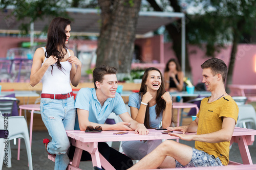 A company of good-looking friends is laughing, socialising and sitting at the table in the nice summer cafe. Entertainment, having good time. Friendship.