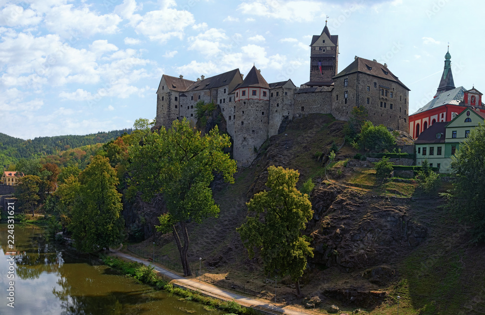 Panorama of Loket Castle at the top of the rocky hill with Ohre River and colorful medieval buildings by summer sunny day. Bohemia, Sokolov, Karlovarsky Region, Czech Republic