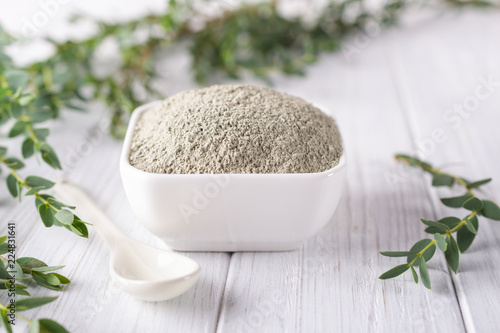 Ceramic bowl with green clay powder and fresh eucalyptus leaves on white background. Concept of face and body care.