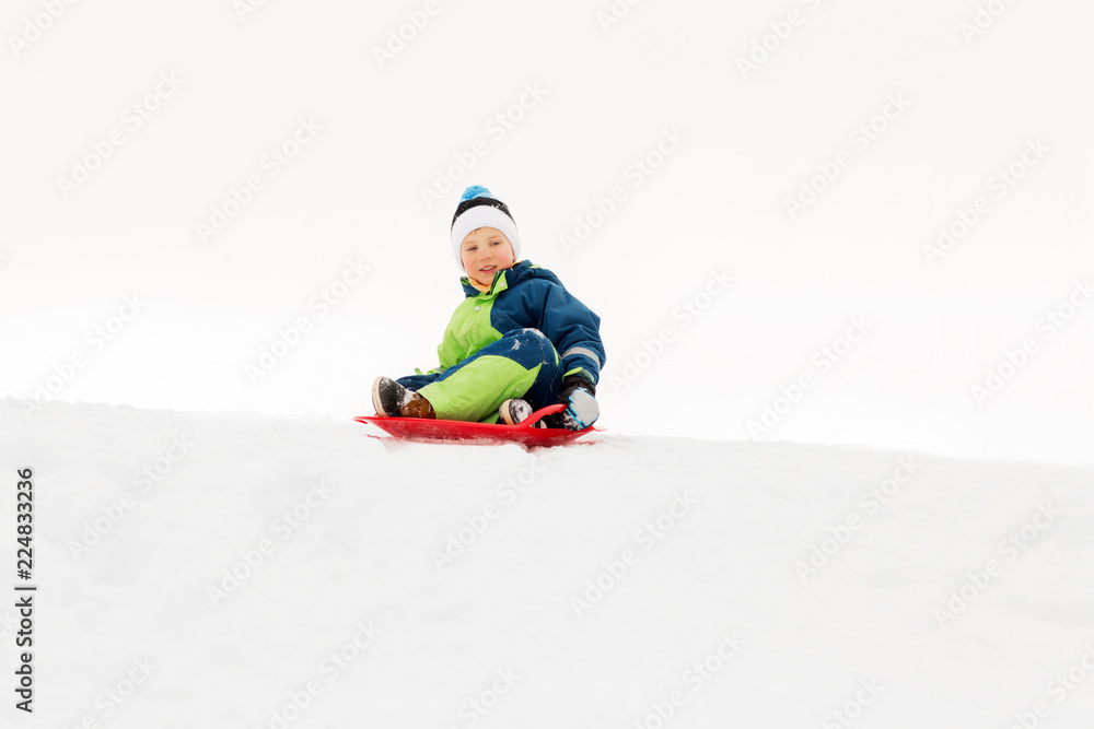 childhood, sledging and season concept - happy little boy sliding on sled down snow hill outdoors in winter childhood, sledging and season concept - happy little boy sliding on sled down snow hill outdoors in winter