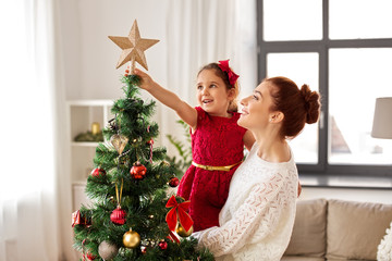 family, winter holidays and people concept - happy mother and little daughter decorating christmas tree at home