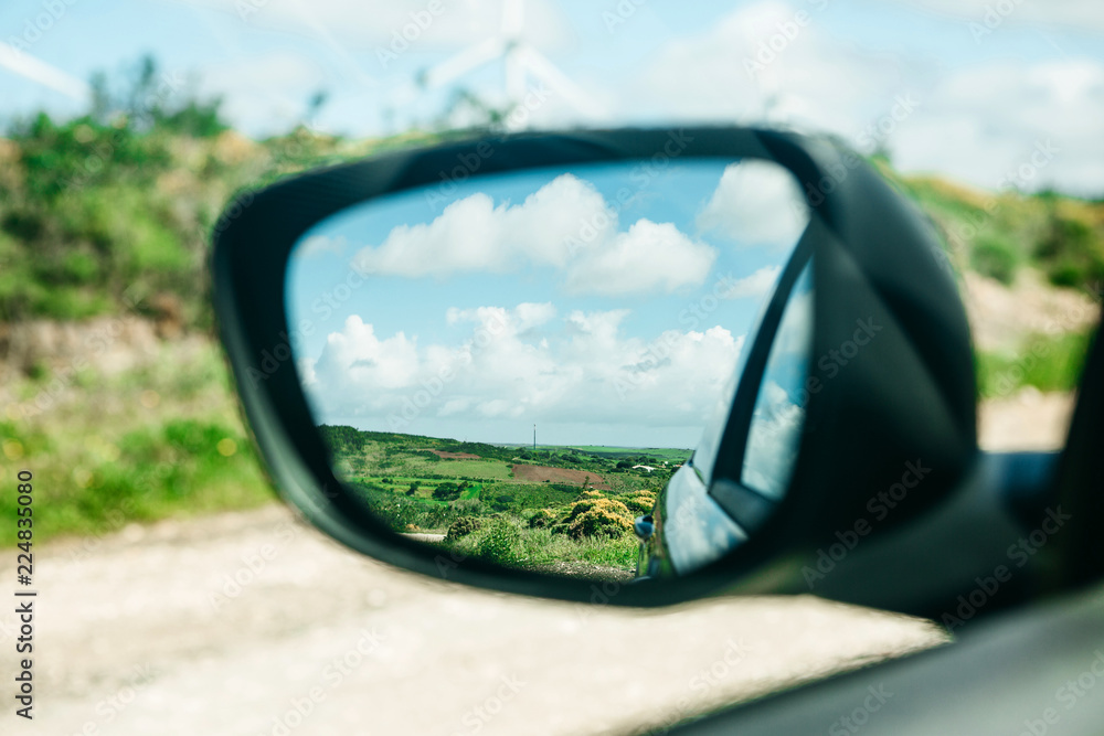 Close-up of a car rear view mirror in which a beautiful blue sky and a rural landscape. Traveling in the countryside.