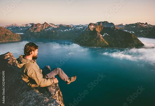 Man tourist sitting alone on the edge cliff mountains above sea travel adventure lifestyle extreme vacations in Norway