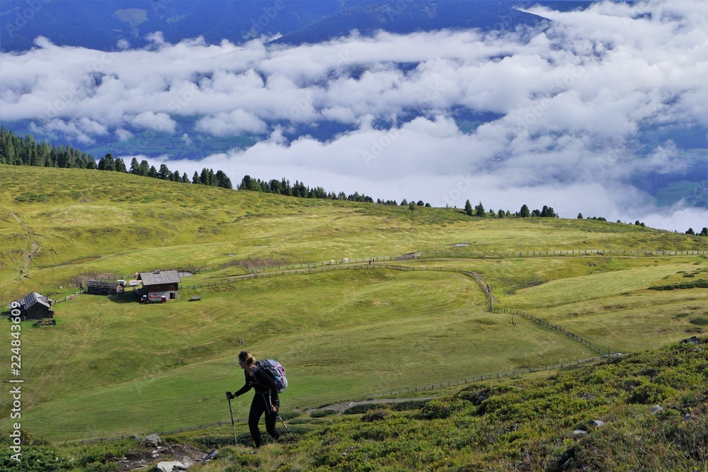 Hiker on a green meadow in the mountains with a hut hiking