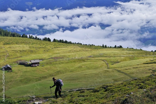Hiker on a green meadow in the mountains with a hut hiking