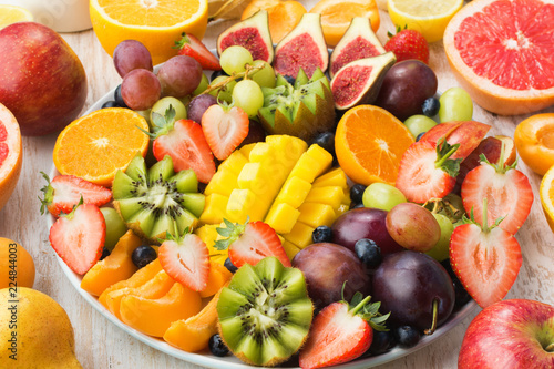 Variety of cut fruits and berries platter  strawberries blueberries  mango orange  apple  grapes  kiwis on the white wood background  copy space for text  vertical  close up  selective focus