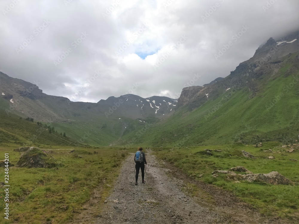 Hiker girl walking on a stone and snow field in the mountains with backpack