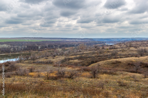The autumn landscape with grassland on the foreground and the river and forest at the distance