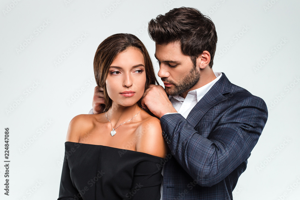 Perfect gift from loving man. Loving men putting necklace to his girlfriend while standing against white background Perfect gift from loving man. Loving men putting necklace to his girlfriend while standing against white background