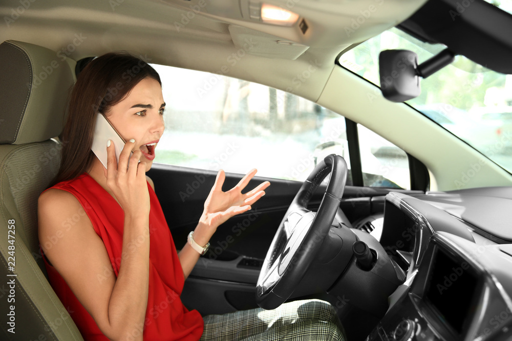 Displeased young woman talking by mobile phone on driver's seat of car