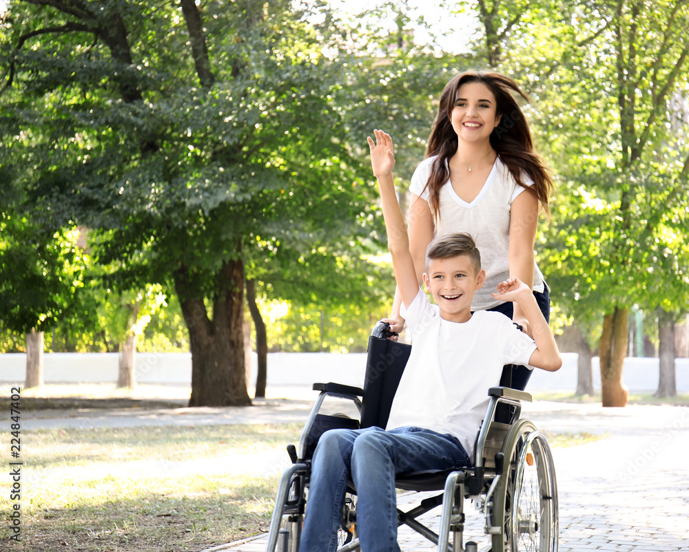 Teenage boy in wheelchair with his mother walking outdoors Teenage boy in wheelchair with his mother walking outdoors