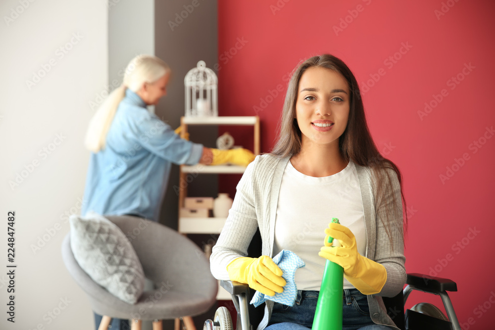Young woman in wheelchair with cleaning detergent and cloth at home
