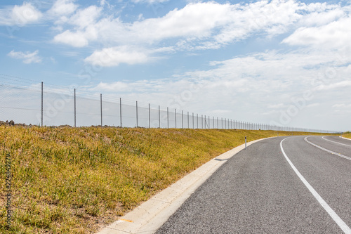 Meshwire fence line along road beneath cloudy sky photo