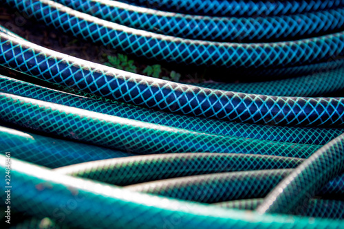 Green long hose pipe lying at the ground at natural background with bokeh