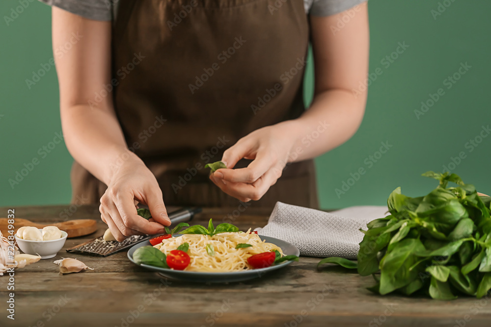 Woman decorating adding fresh basil to tasty pasta