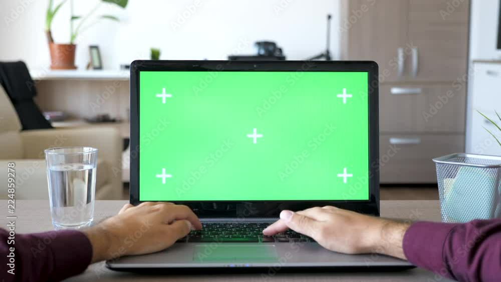POV of man typing on laptop with green screen chroma mock up. He is in his living room in the house. First person view