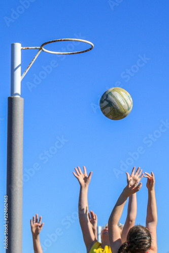 Netballers jumping for ball against blue sky