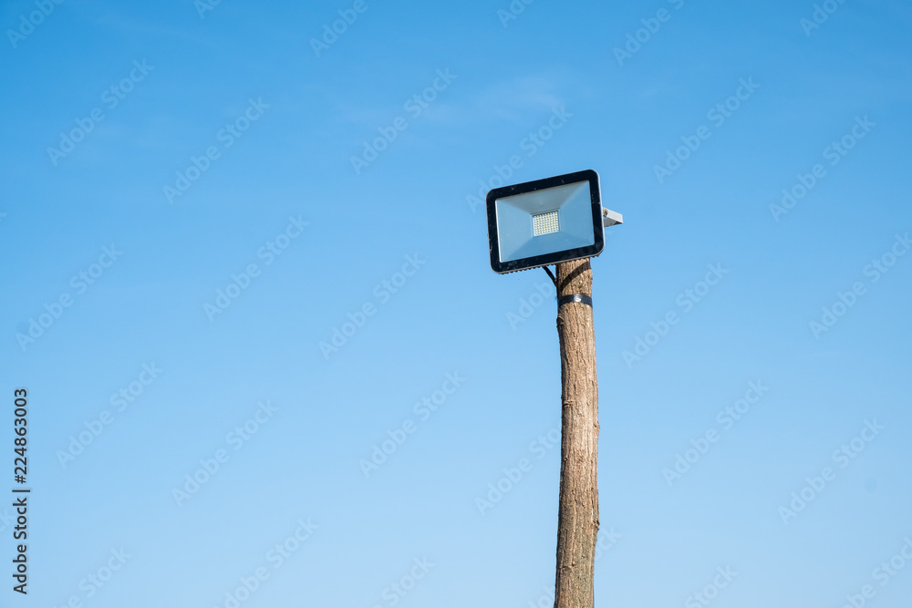 led street lamp mounted on a wooden tree trunk against a blue sky led street lamp mounted on a wooden tree trunk against a blue sky