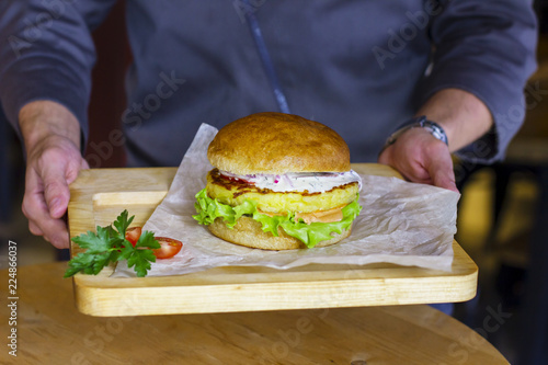 Vegetarian Burger with potato cutlet  salad and sauce on wooden Board in male hands