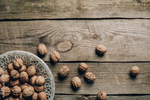 top view of ripe organic walnuts and plate on wooden table