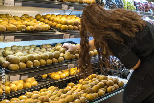 Fresh healthy fruits on shelves in supermarket. With a woman choosing best fruits