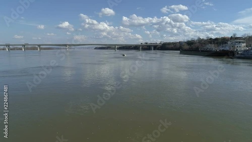 A man driving a boat fast. Middle of the river. Camera flies towards it. Bridge in the background. Cloud reflects on the water. photo