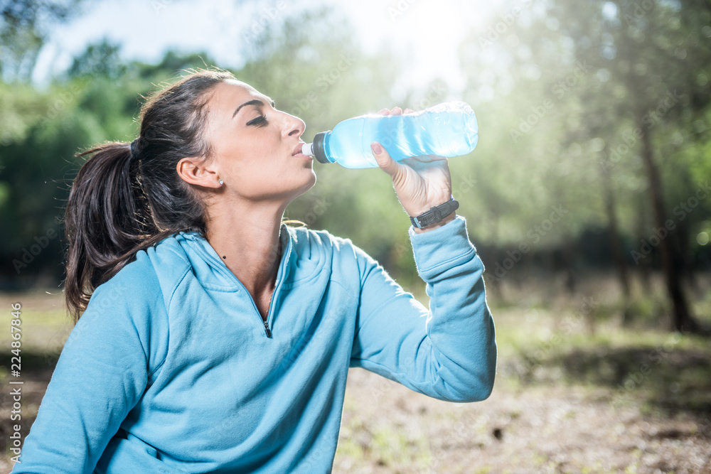 Young woman resting and drinking from a plastic bottle after running Young woman resting and drinking from a plastic bottle after running