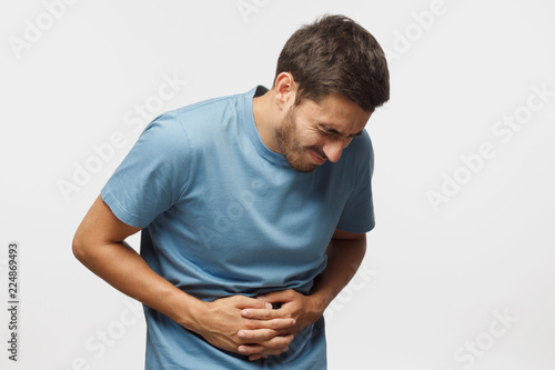 Young man touching his stomach isolated on gray background space. Abdominal pain or ache concept