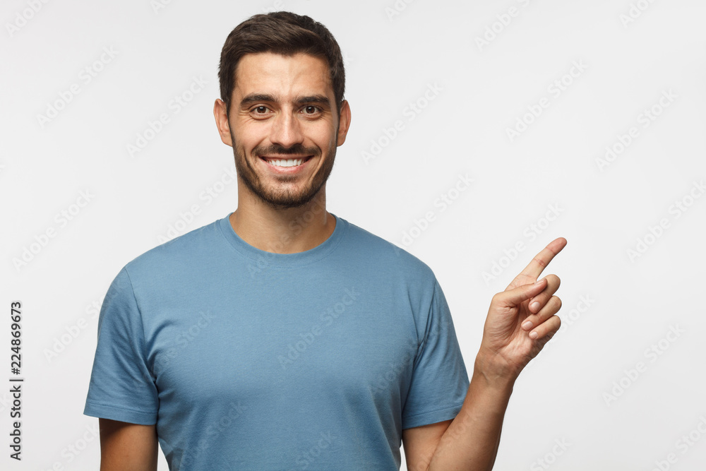 Handsome smiling male in blue t-shirt pointing right with finger isolated on gray background Handsome smiling male in blue t-shirt pointing right with finger isolated on gray background