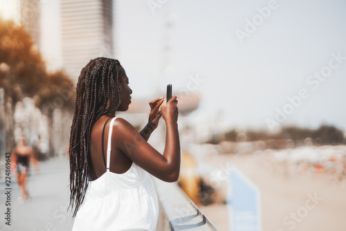 Photography Cute black girl in a white dress is photographing sea and beach using the camera
