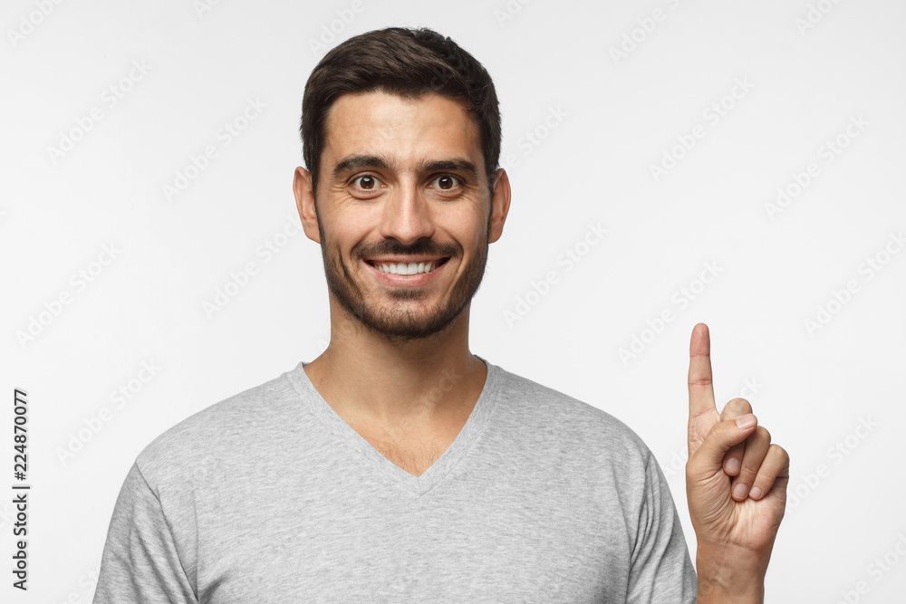 Handsome young man pointing up with his index finger, isolated on gray background Handsome young man pointing up with his index finger, isolated on gray background