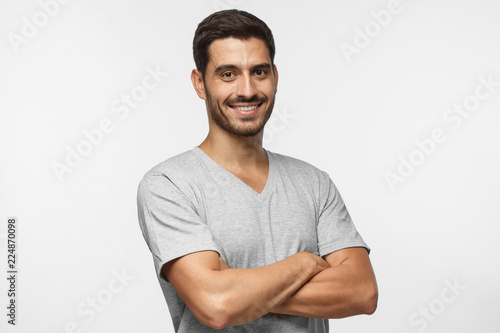Portrait of attractive young sporty man in gray t-shirt standing with crossed arms isolated on grey background