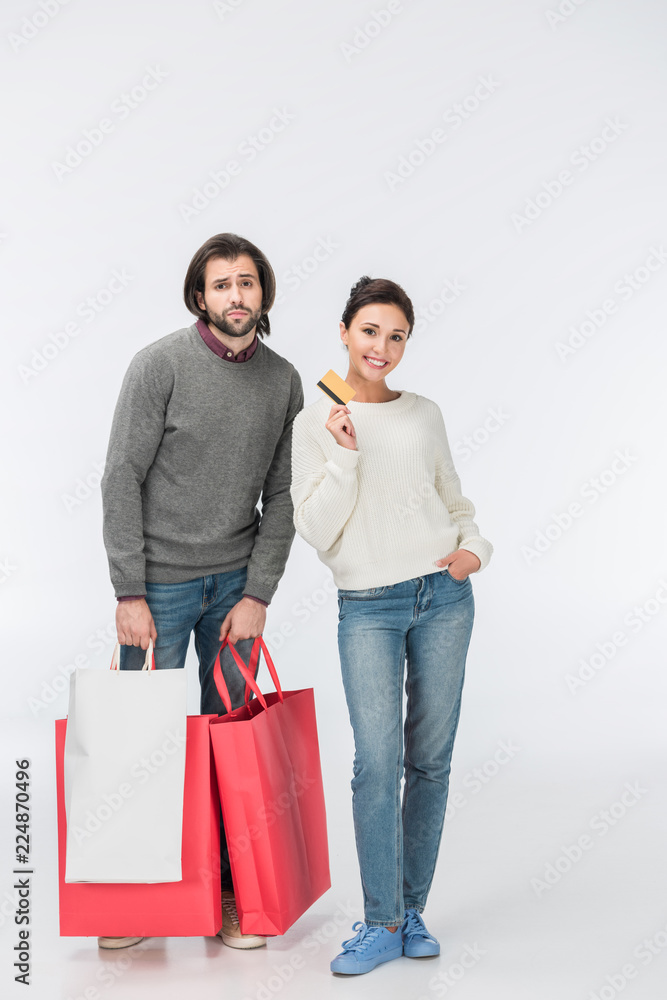 thoughtful man with shopping bags and smiling woman showing credit card isolated on white thoughtful man with shopping bags and smiling woman showing credit card isolated on white