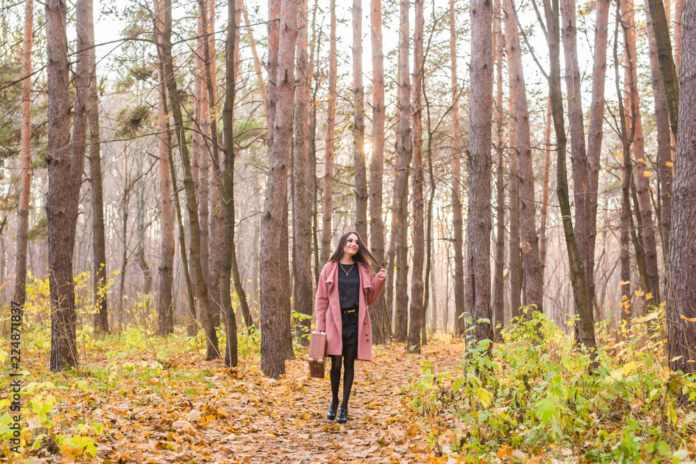 Autumn, fashion, people concept - woman with brown retro suitcase walking through the autumn park and smiling Autumn, fashion, people concept - woman with brown retro suitcase walking through the autumn park and smiling